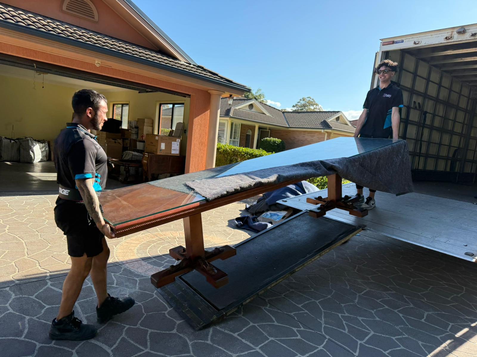 Two removalists carrying a timber table from a home to the moving truck